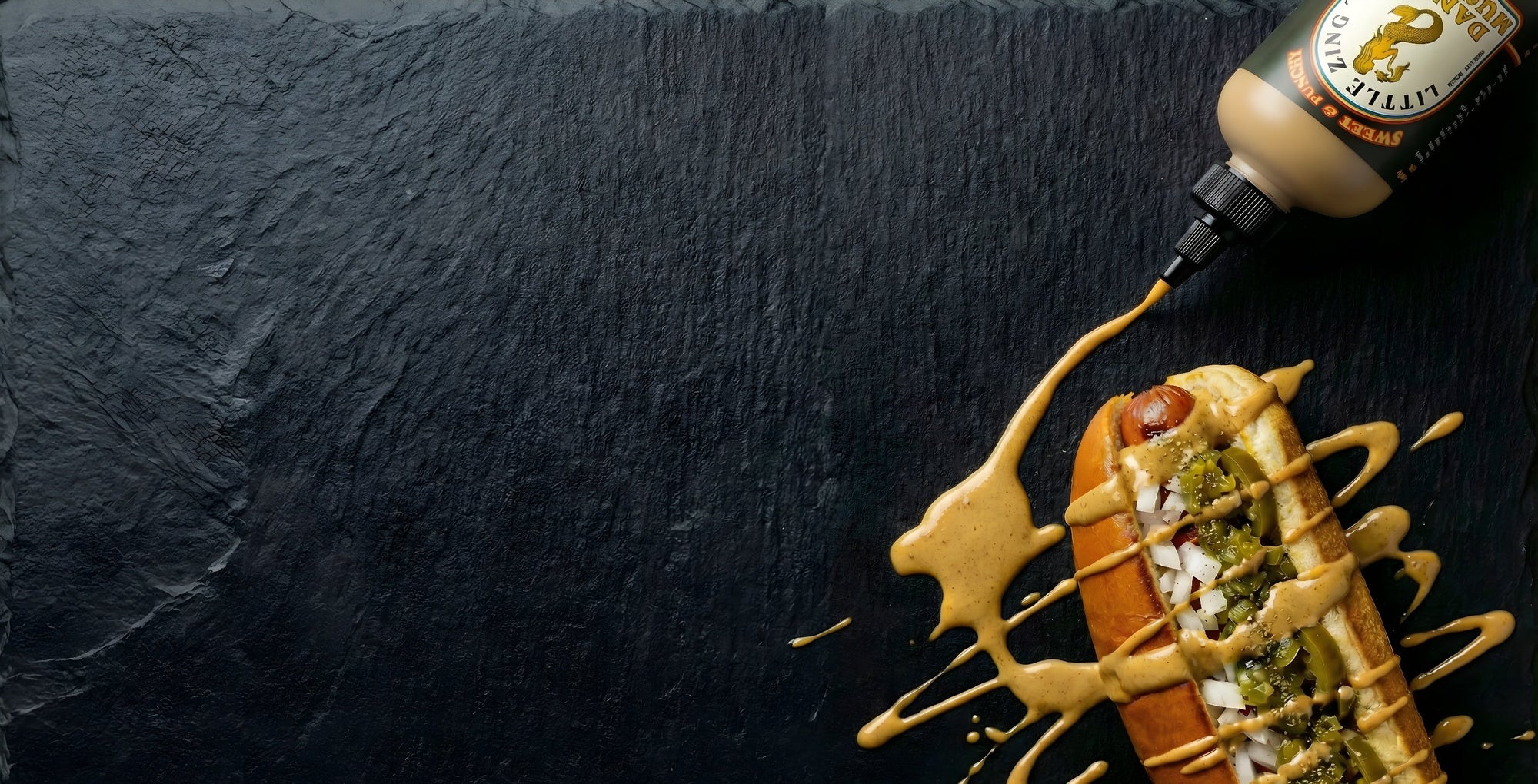 Hot dog with mustard and relish on a dark surface with a bottle of mustard.