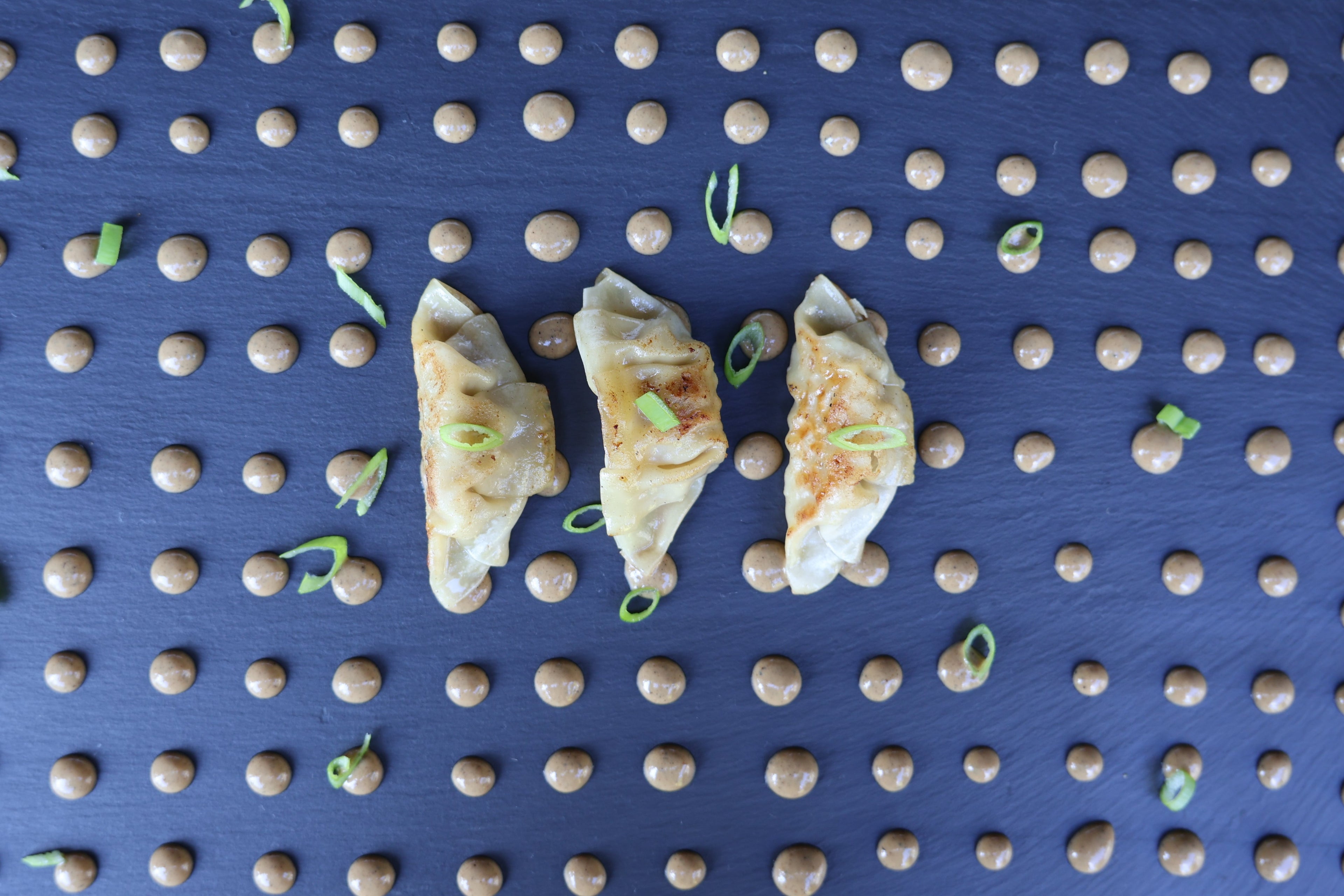 Three dumplings with green onions on a pegboard background