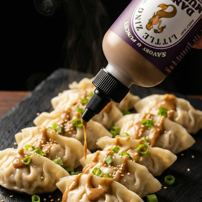 Dumplings on a black slate board with a bottle of sauce being poured over them.